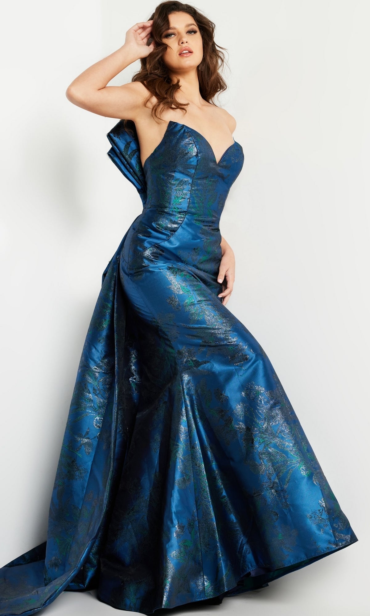 A woman poses in the Jovani 23898 Navy Blue Long Formal Dress featuring a shiny strapless design, sweetheart neckline, fitted bodice, flared skirt, and a large bow detail at the back.